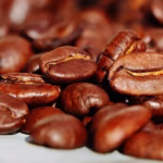 Grãos de café torrados em close detalhado, com foco em grãos inteiros de coloração marrom escura e brilhante. Foto macro ideal para ilustrar o mercado de café e a produção agrícola no portal CotaboiBrasil.